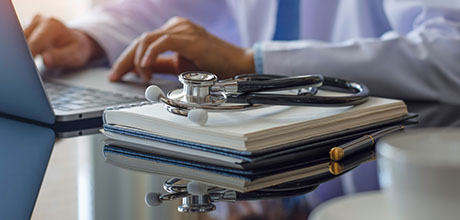physician on laptop with files and stethoscope