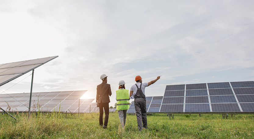 3 workers wearing safety vests looking at solar panels under a blue sky
