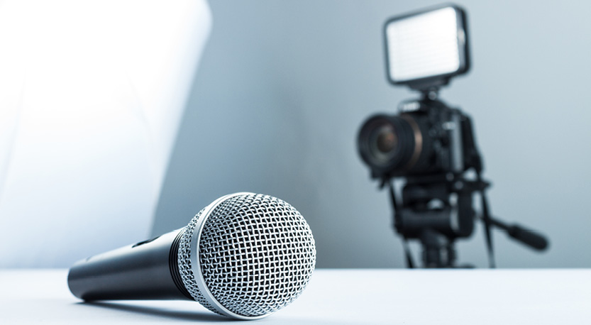 A microphone lays on a table in front of a video camera