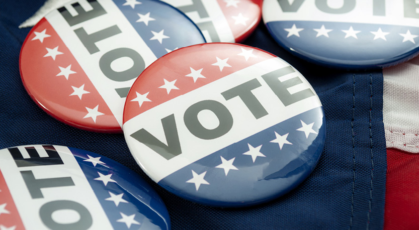 5 buttons reading VOTE lay across a red, white, and blue fabric.